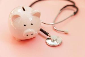 medicin läkare utrustning stetoskop och spargris isolerad på rosa pastell bakgrund. hälsovård finansiell kontroll eller spara för sjukförsäkring kostnader koncept. kopieringsutrymme. foto