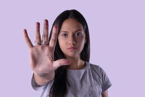 ung latinsk kvinna i casual outfit gör handen stoppskylt mot lila studio bakgrund. foto