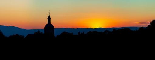 den fantastiska skönheten och färgerna i solnedgången med utsikt över alpernas silhuetter och silhuetten av en vacker kyrka foto