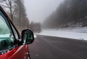 röd bil på vintervägen i bergen, skog med snö foto