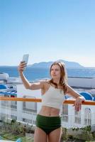 glad kvinna i baddräkt tar selfie stående på balkongen i hotellrummet foto