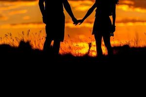 vackra unga par står solnedgången. två håller varandra i handen. naturskön landskapsvy med solnedgång. foto