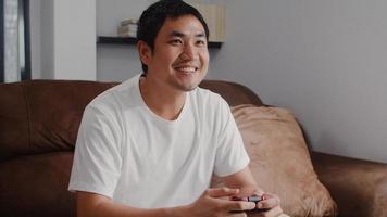 ung asiatisk man som använder joystick som spelar videospel i tv i vardagsrummet, en man som känner sig nöjd med att koppla av när han ligger på soffan hemma. män spelar spel koppla av hemma koncept. foto