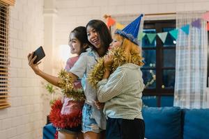 grupp asiatiska kvinnor festar hemma, kvinnor använder mobiltelefon och gör vloggar och selfie till sociala medier medan roliga ögonblick dansar tillsammans i vardagsrummet på natten. ung vän fira semester koncept foto