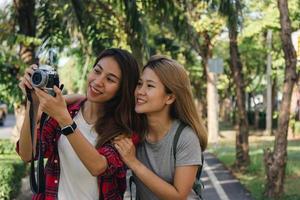 glad vacker resenär asiatisk vän kvinnor bär ryggsäck. unga glada vän asiatiska kvinnor som använder kameran för att göra foto under stadsrundtur, glada känslor. kvinnor livsstil utomhus i staden koncept.