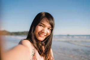 turist asiatisk kvinna selfie på stranden, ung vacker kvinna glad leende med hjälp av mobiltelefon tar selfie på stranden nära havet när solnedgången på kvällen. livsstil kvinnor reser på stranden koncept. foto