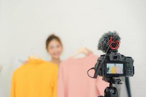 asiatisk mode kvinnlig bloggare online influencer håller shoppingkassar och massor av kläder på klädhängare för inspelning av ny modevideo sänds livevideo till socialt nätverk via internet hemma. foto