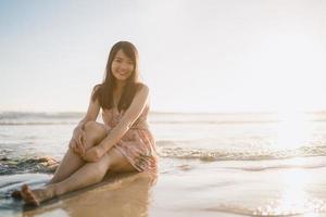 ung asiatisk kvinna känner sig glad på stranden, vacker kvinna glad slappna av leende roligt på stranden nära havet när solnedgången på kvällen. livsstil kvinnor reser på stranden koncept. foto