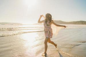 ung asiatisk kvinna springer och leker på stranden, vacker kvinna koppla av på stranden nära havet när solnedgången på kvällen. livsstil kvinna resa på stranden koncept. foto