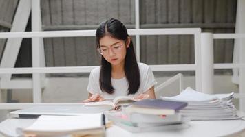 asiatiska studentkvinnor som läser böcker i biblioteket på universitetet. ung flicka på grundutbildningen gör läxor, läser lärobok, studerar hårt för kunskap och utbildning på föreläsningsbänken på universitetsområdet. foto