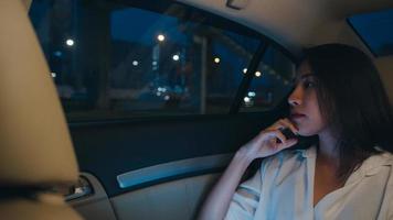 framgångsrik ung asiatisk affärskvinna i mode kontorskläder som arbetar sent med smart telefon i sittande baksäte på bilen i urban modern stad på natten. människor yrkesmässigt utbrändhetssyndrom koncept. foto