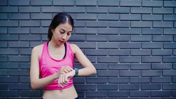 hälsosam vacker ung asiatisk idrottsman kvinna inställning och kontrollera framsteg ser pulsmätare på smart klocka medan du kör i urban stad. livsstilskvinnor tränar i stadskonceptet. foto