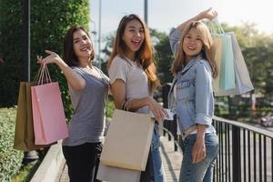 grupp av ung asiatisk kvinna som shoppar på en utomhusmarknad med shoppingkassar i händerna. unga asiatiska kvinnor visar vad de fick i shoppingväskan under varmt solljus. grupp utomhus shopping koncept. foto
