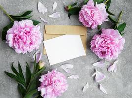 inbjudningskort, pysselkuvert och rosa pionblommor foto