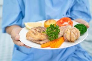 asiatisk senior eller äldre gammal dam kvinna patienten äter frukost och grönsaker hälsosam mat med hopp och glad medan du sitter och hungrig på sängen på sjukhuset. foto