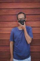asiatisk man bär skydd ansiktsmask stående mot trävägg foto