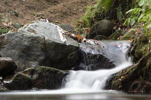 fallna löv i det steniga vattenfallet. den steniga bäcken matar in längs floden. vattenfall i skogen. vackert skogs- och flodlandskap. foto