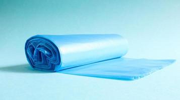 en rulle plastsoppåsar i blått på blå bakgrund. påsar som är designade för att rymma sopor i dem och används hemma och placeras i olika sopkärl. foto