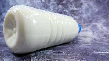 en plastflaska med ett blått lock med färsk vanlig mjölk på en mörkgrå marmorerad eller betongbakgrund. närbild framifrån. världens mjölkdag koncept. näringsvätska. foto