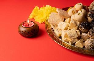 traditionella indiska godis på röd bakgrund med ljus och blommor platt låg foto