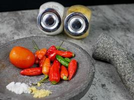 röd chili, tomater och kryddor i en mortel är redo att göra chilisås. matlagning koncept foto