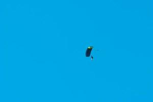 tandem fallskärmshopp. siluett av fallskärmshoppare flyger i blå klar himmel. foto
