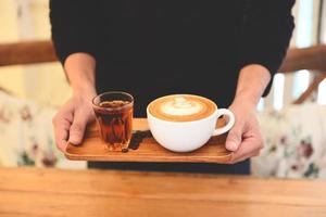 kaffekopp i handen på träbord i café med kaffebönor bakgrund, serverad kaffe cappuccino eller latte och te. foto