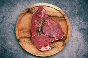 färskt nötkött animaliskt protein rått nötkött med rosmarin på träplatta i köket för att laga nötbiff stekt eller grillad med ingredienser ört foto