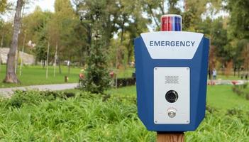 nödknapp i en offentlig stadspark med ett engelskt ord nödsituation. sos, polis, panik. människor säkerhetskoncept. nödrop på hjälp. foto