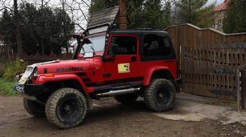 Ukraina, Yaremche - 20 november 2019. en röd jeep Wrangler 4.0i v6 suv är parkerad på en landsväg nära ett hus i en liten stad i ukrainska Karpaterna. utflykter berg jeep ride. foto