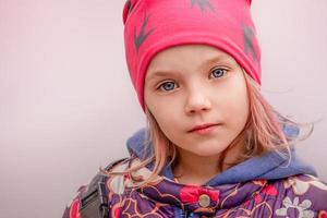 flicka med rosa hår i en keps och i en blommig jacka. liten flicka med blå ögon. foto