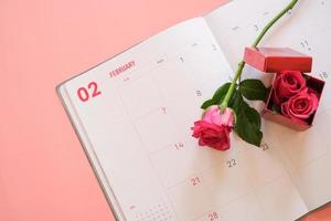 rosa ros och röd presentförpackning på kalenderboken isolerad på rosa bakgrund med copyspace för text. alla hjärtans dag koncept. planering schemaläggning agenda, evenemang, arrangör alla hjärtans dag. foto