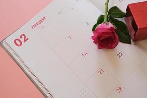 rosa ros och röd presentförpackning på kalenderboken isolerad på rosa bakgrund med copyspace för text. alla hjärtans dag koncept. planering schemaläggning agenda, evenemang, arrangör alla hjärtans dag. foto