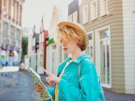 rödhårig ung kvinna reser över Västeuropa och använder papperskarta i okänd stad. resefoto. förlorade i ny stad foto