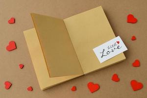 öppen bok, anteckningsbok gjord av kraftpapper, kort med kärlek, röda hjärtan på bordet. alla hjärtans dag-kort foto