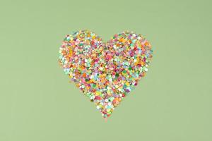 hjärtform gjord av mångfärgad papperskonfetti på en grön bakgrund. kreativa alla hjärtans dag-kort foto