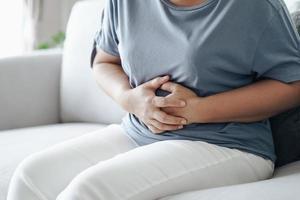 kvinna som lider av magvärk sitter i soffan hemma. buksmärtor, gastrit, mens, menstruation. foto