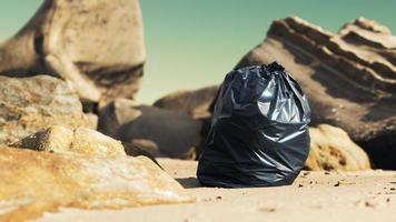 svart plastsoppåse full av skräp på stranden foto