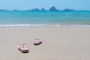 rosa strandpromenad tofflor eller sandlar av ung kvinna som placerar på vit strand och blått hav på sommarlovet. resekoncept foto