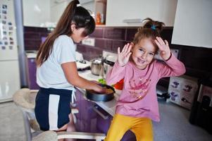 mamma med flicka matlagning i köket, glada barns stunder. foto