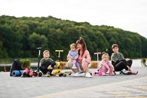 ung snygg mamma med fyra barn utomhus. sportfamiljen tillbringar fritid utomhus med skotrar och skridskor. foto