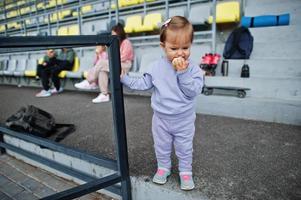 flicka äta äpple. ung snygg mamma med fyra barn som sitter på sportpallen på stadion. familjen tillbringar fritid utomhus med skotrar och skridskor. foto