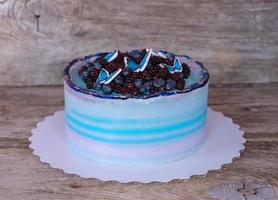 vacker hembakad tårta med lila och blå grädde, dekorerad med björnbär, blåbär och fjärilar foto
