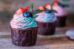 hemgjorda cupcakes med rosa och turkos grädde, dekorerade med jordgubbar och blåbär foto