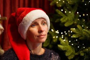 porträtt av en söt kvinna i en jultomtehatt nära granen foto