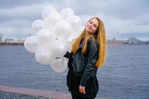 kaukasisk flicka håller vita ballonger stående vid floden på vallen av staden foto