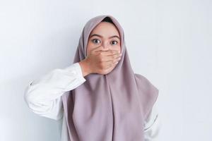 ung asiatisk islam kvinna som bär huvudduk är chockad med händerna som täcker hennes mun. indonesisk kvinna på grå bakgrund foto