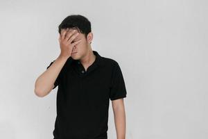 porträtt av ung asiatisk man isolerad på grå bakgrund som lider av svår huvudvärk, trycker fingrarna mot tinningarna, sluter ögonen för att lindra smärta med hjälplöst ansiktsuttryck foto