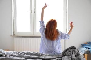 ung kvinna sträcker sig efter att ha vaknat och stigit ur sängen foto