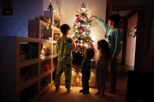 barn tittar på julgran med lysande girlander på kvällen hemma. foto